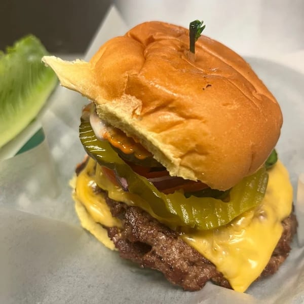A Halal Buns cheeseburger with pickles, onions, and sauce, served on a bun with a side of lettuce.