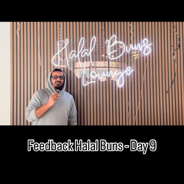 Man in a grey hoodie holding a microphone in front of a neon "Halal Buns Lounge" sign.