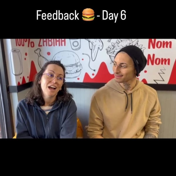 Two people, a woman and a man, sitting in Halal Buns restaurant with a burger mural behind them.
