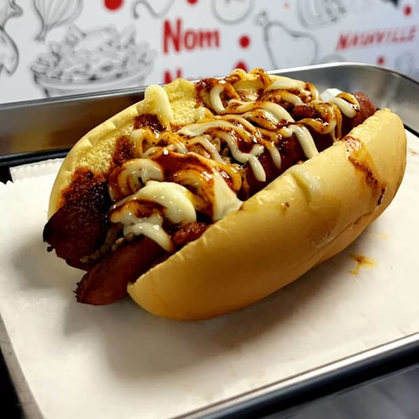 A Halal Buns hot dog with chili, white sauce, and barbecue sauce on a bun.