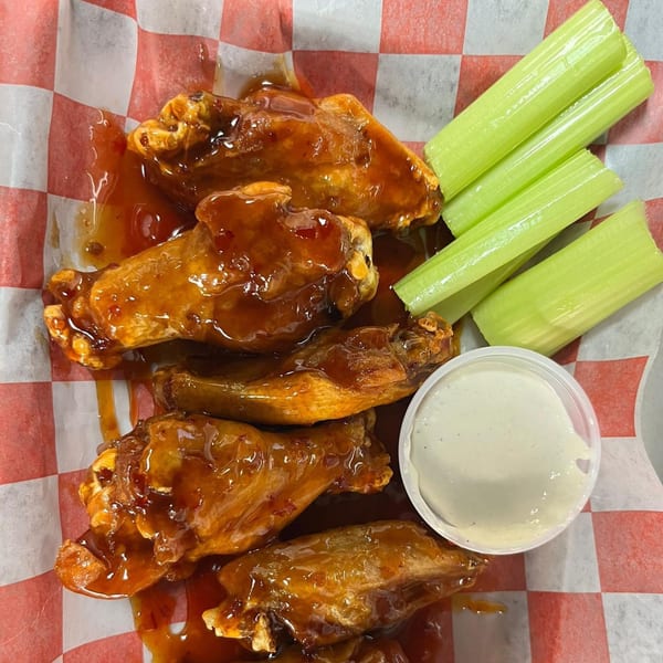 Sweet and spicy Halal Buns chicken wings with celery sticks and ranch dressing on checkered paper.