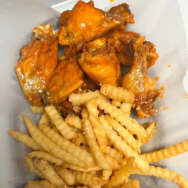 A basket of Halal Buns' American-style hot wings with crinkle-cut fries on white paper.