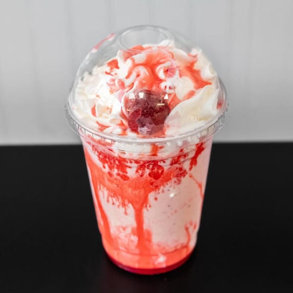 Strawberry milkshake with whipped cream, red syrup, and a cherry on top, from Halal Buns.