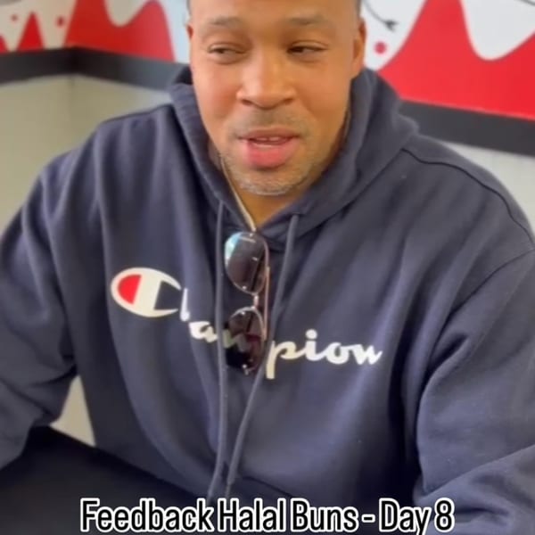 A man in a Champion hoodie with sunglasses hanging from his neck, talking at Halal Buns.