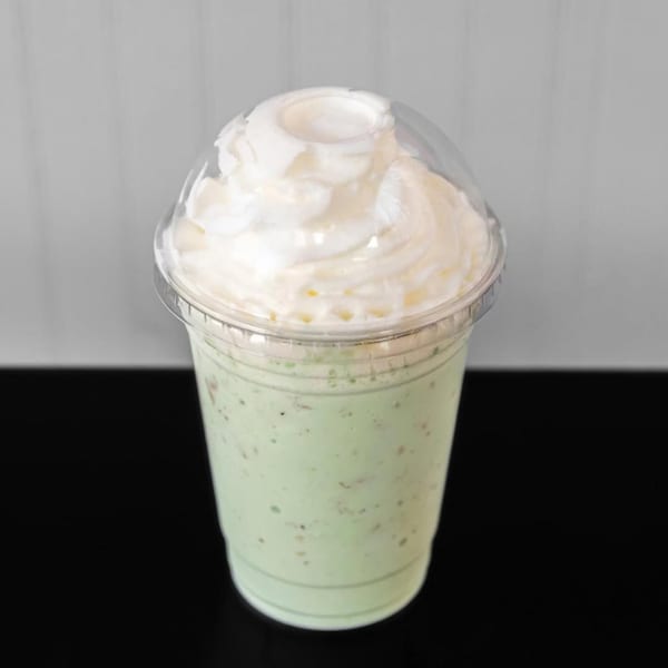 A light green milkshake with whipped cream on top, in a clear plastic cup.