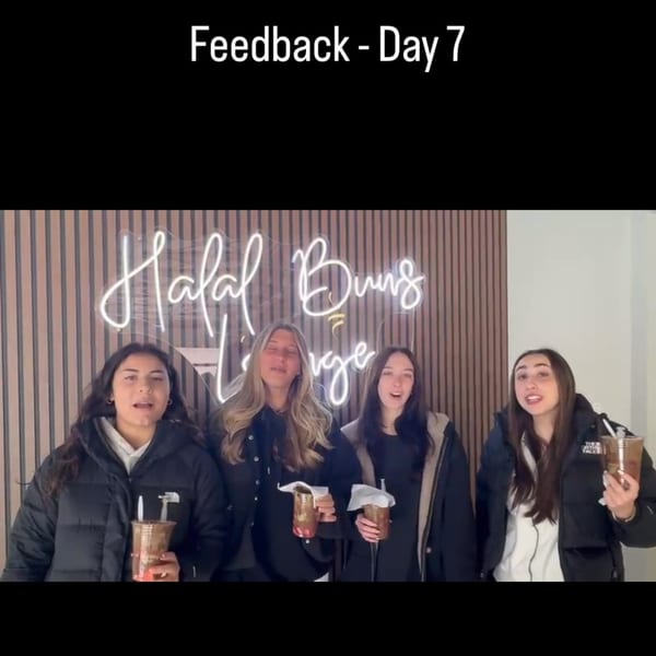 Four young women holding drinks, standing in front of a neon "Halal Buns Lounge" sign.