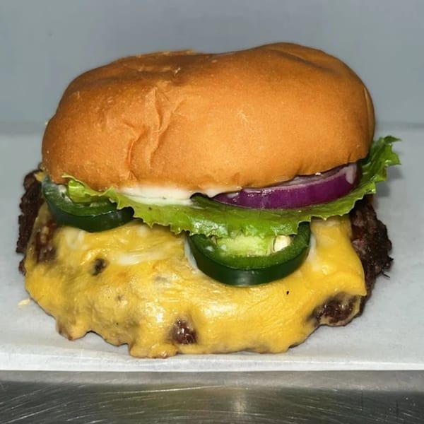 A Halal Buns cheeseburger with melted cheese, lettuce, red onion, and jalapeños on a bun.