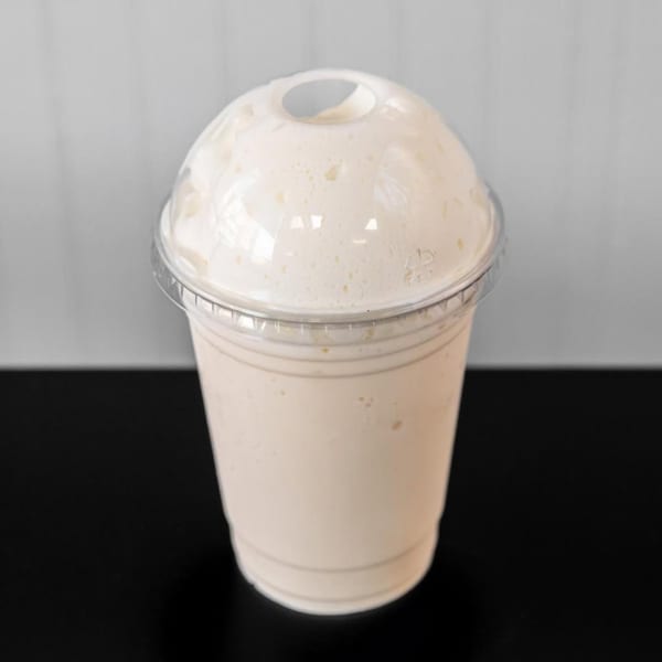 A creamy vanilla milkshake in a clear plastic cup with a domed lid, from Halal Buns.
