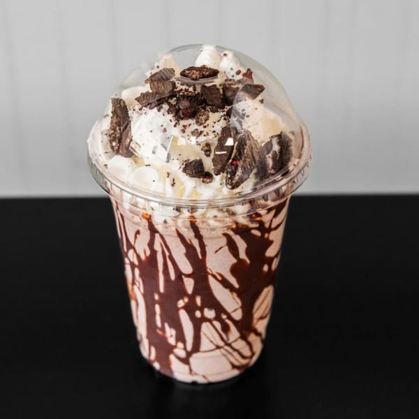 A Halal Buns milkshake in a clear cup, topped with whipped cream and chocolate cookie crumbles.