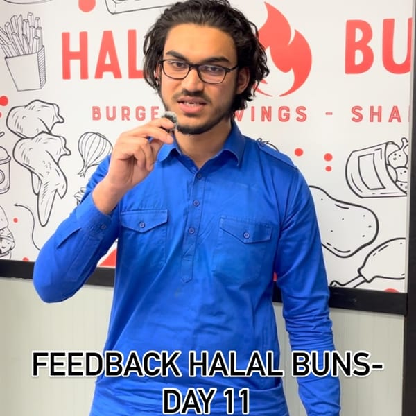 A man in a blue shirt and glasses speaks into a microphone in front of a Halal Buns wall.