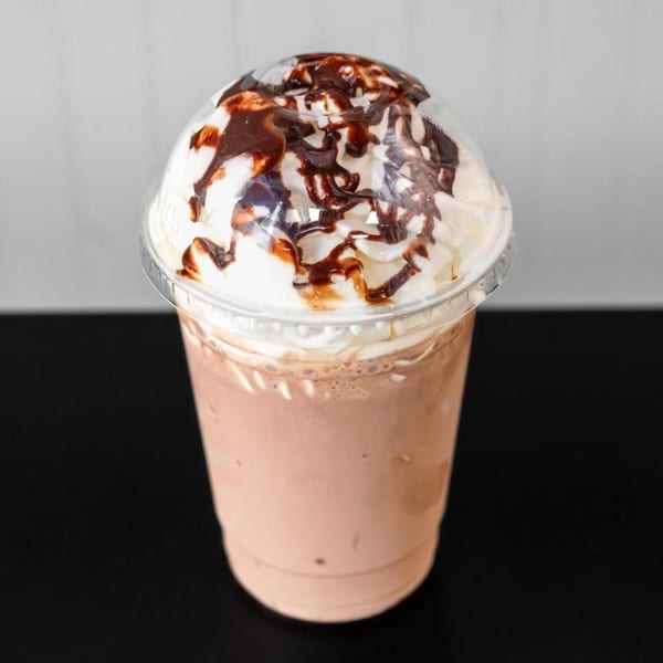 A chocolate milkshake with whipped cream and chocolate syrup in a clear plastic cup.